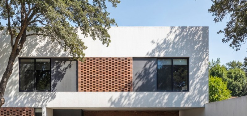 Vivienda de dos plantas con celosía de ladrillo entre árboles